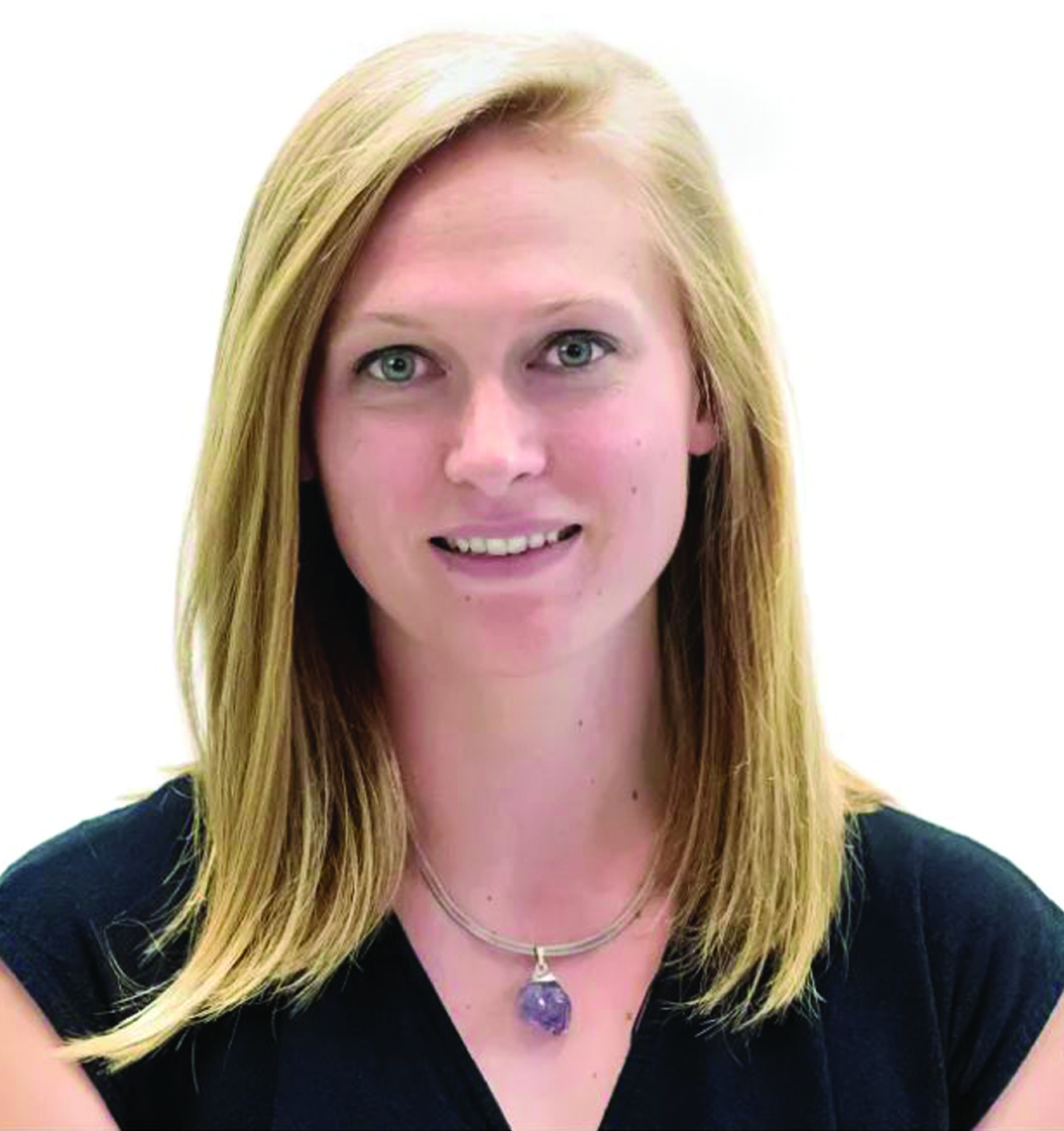 Portrait of a smiling woman with blonde hair, wearing a black top and a necklace with a purple pendant.